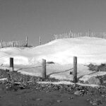 black and white image of a dune with snow on it and fencint